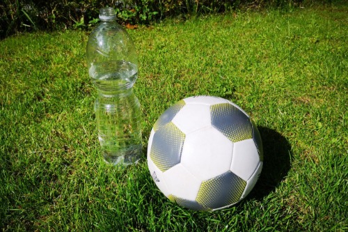 Fles gevuld met water en een voetbal op het gras